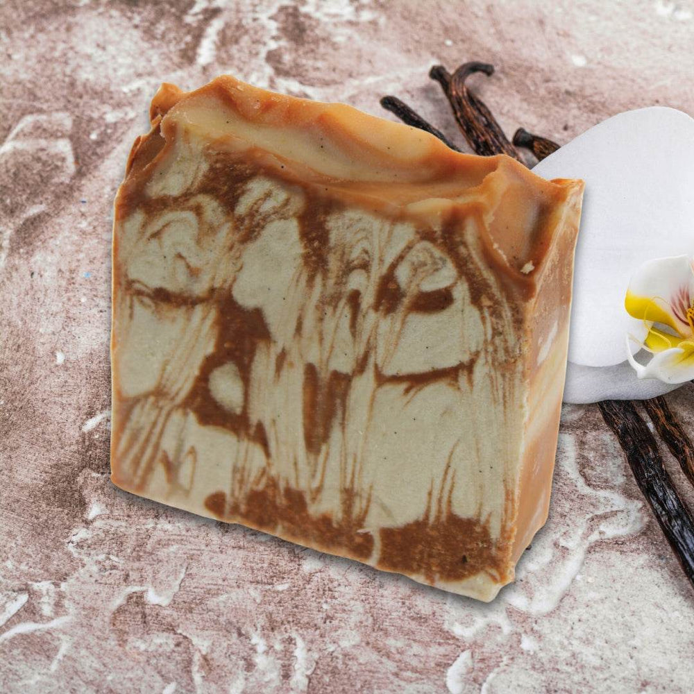 Vanilla Bean & Clay Soap with marbled texture on a natural background featuring vanilla beans and a flower.