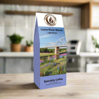 Front view of EarthRoast Coffee's Llano River Blend, a light roast specialty coffee. Features a picturesque illustration of the Llano River with a historic bridge, wildflowers, and a bright blue sky, showcasing the organic, sustainably sourced quality of this coffee.